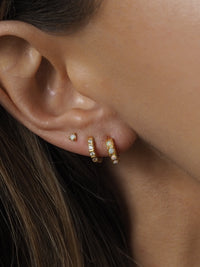 Close-up of three gold earrings worn in a lobe stack: a small opal stud and two gold huggie hoops set with opal and cubic zirconia stones.