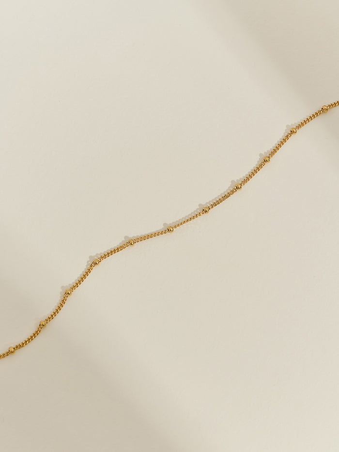 Gold-plated satellite chain bracelet with evenly spaced beaded details, displayed on a neutral background.