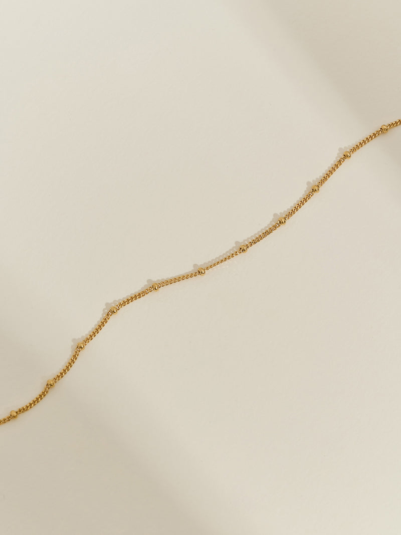 Gold-plated satellite chain bracelet with evenly spaced beaded details, displayed on a neutral background.