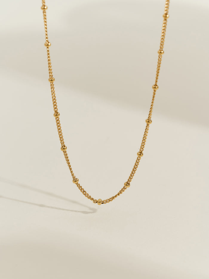 Close-up of a gold-plated satellite chain necklace, featuring evenly spaced tiny gold beads on a delicate chain.