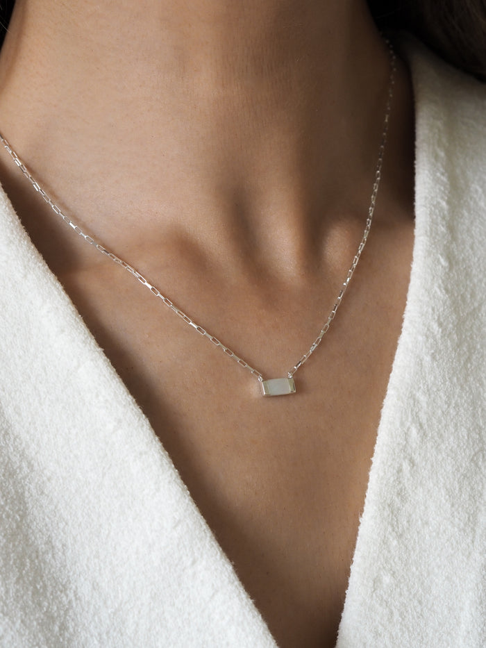 Sterling silver necklace featuring a rectangular mother of pearl pendant, worn with a white textured fabric top.