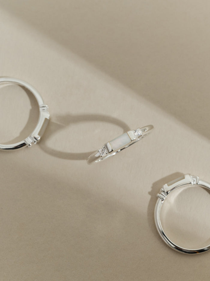 Flat lay of a sterling silver ring with a rectangular mother of pearl stone set between two cubic zirconia stones, shown from multiple angles on a neutral background.