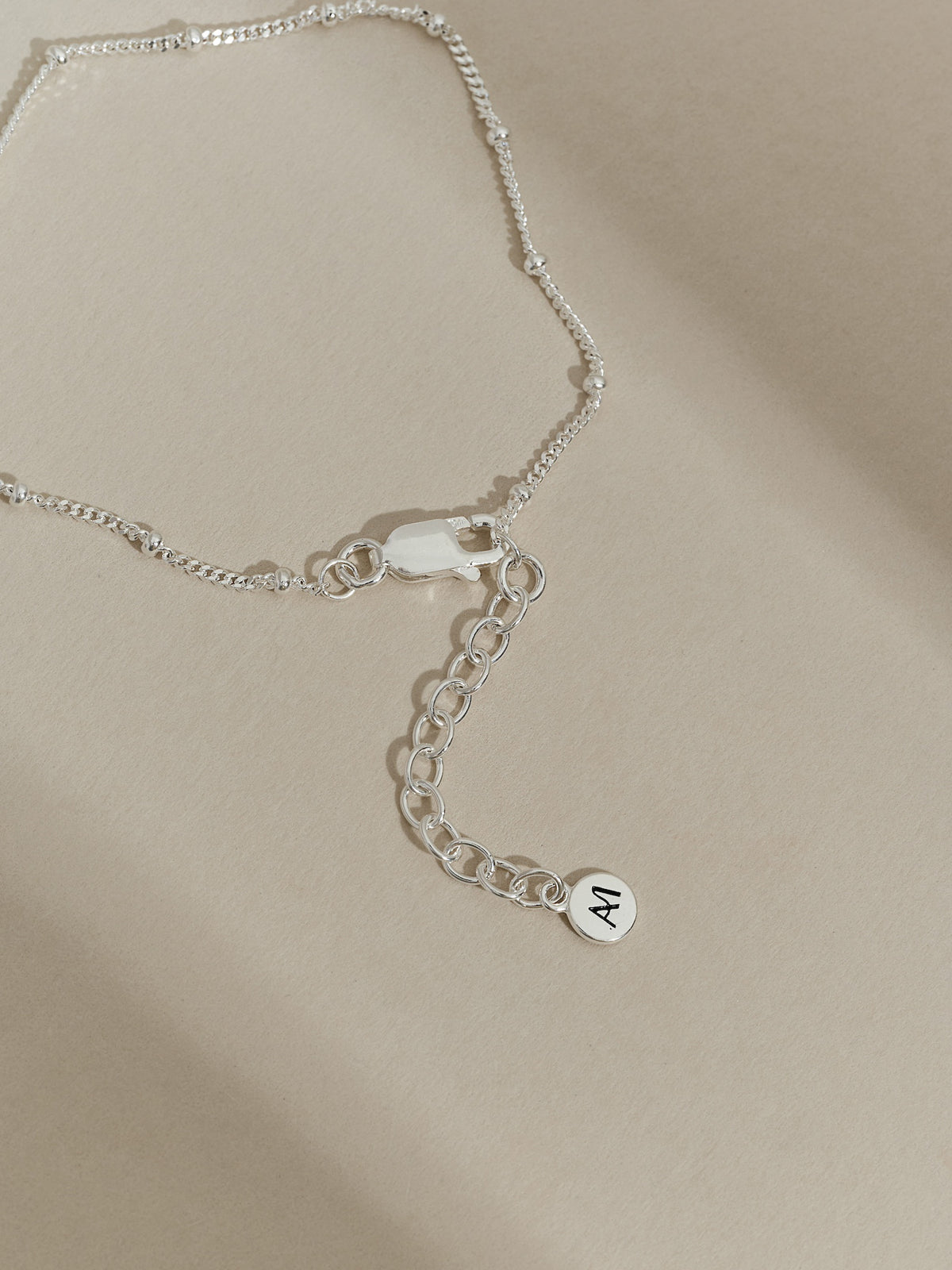 Close-up of the extender chain and clasp of a sterling silver satellite bracelet, finished with an Aluna Mae logo tag.