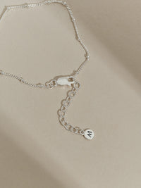 Close-up of the extender chain and clasp of a sterling silver satellite bracelet, finished with an Aluna Mae logo tag.