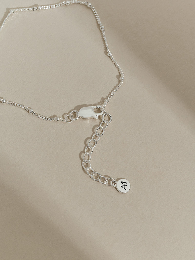 Close-up of the extender chain and clasp of a sterling silver satellite bracelet, finished with an Aluna Mae logo tag.