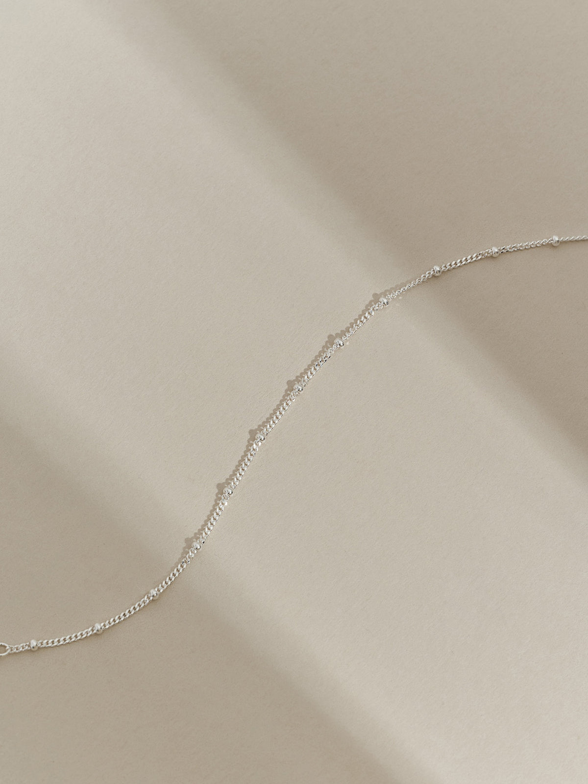 Close-up of a sterling silver satellite chain bracelet photographed in soft natural light on a cream background.