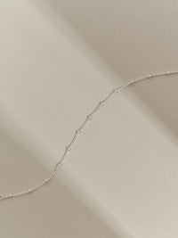 Close-up of a sterling silver satellite chain bracelet photographed in soft natural light on a cream background.