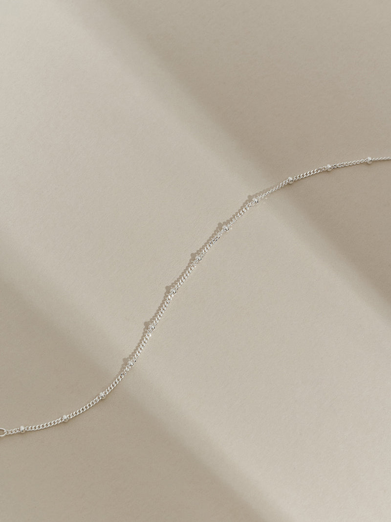 Close-up of a sterling silver satellite chain bracelet photographed in soft natural light on a cream background.