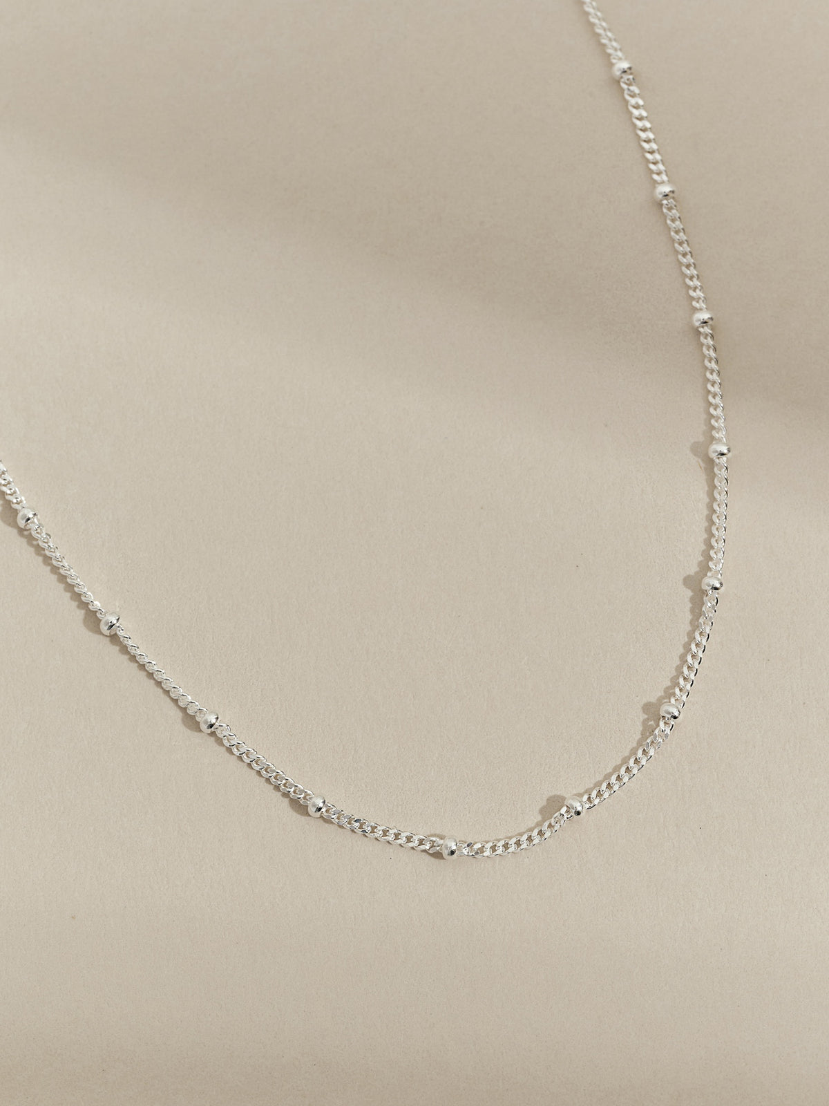 Sterling silver satellite chain necklace displayed on a neutral beige background.
