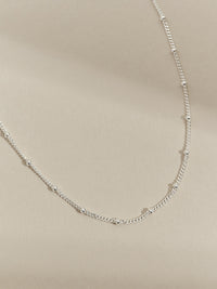 Sterling silver satellite chain necklace displayed on a neutral beige background.