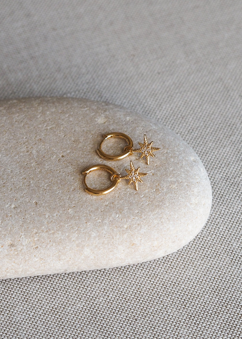 Close-up gold star cubic zirconia hoops displayed on a pebble stone. 