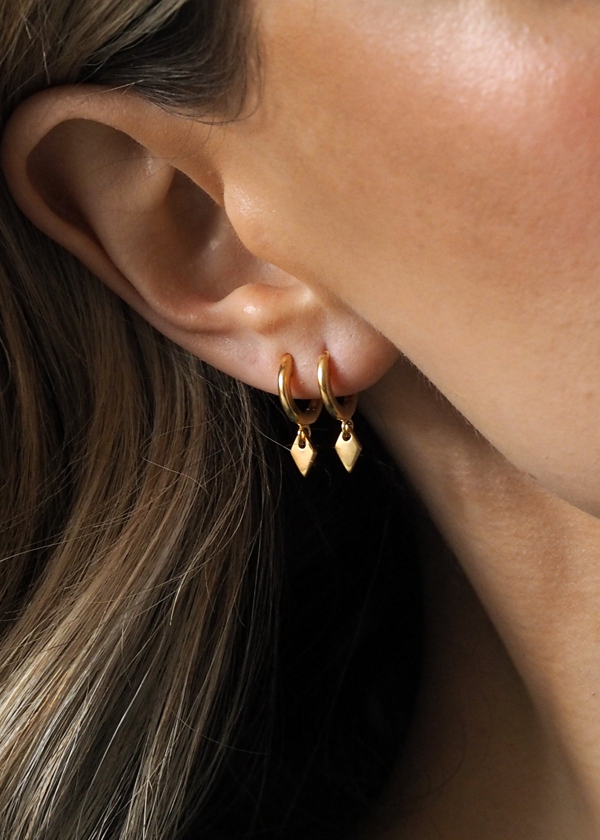 Close-up of a model wearing two gold hoops on one ear. Hoops feature small diamond-shaped drop pendants.