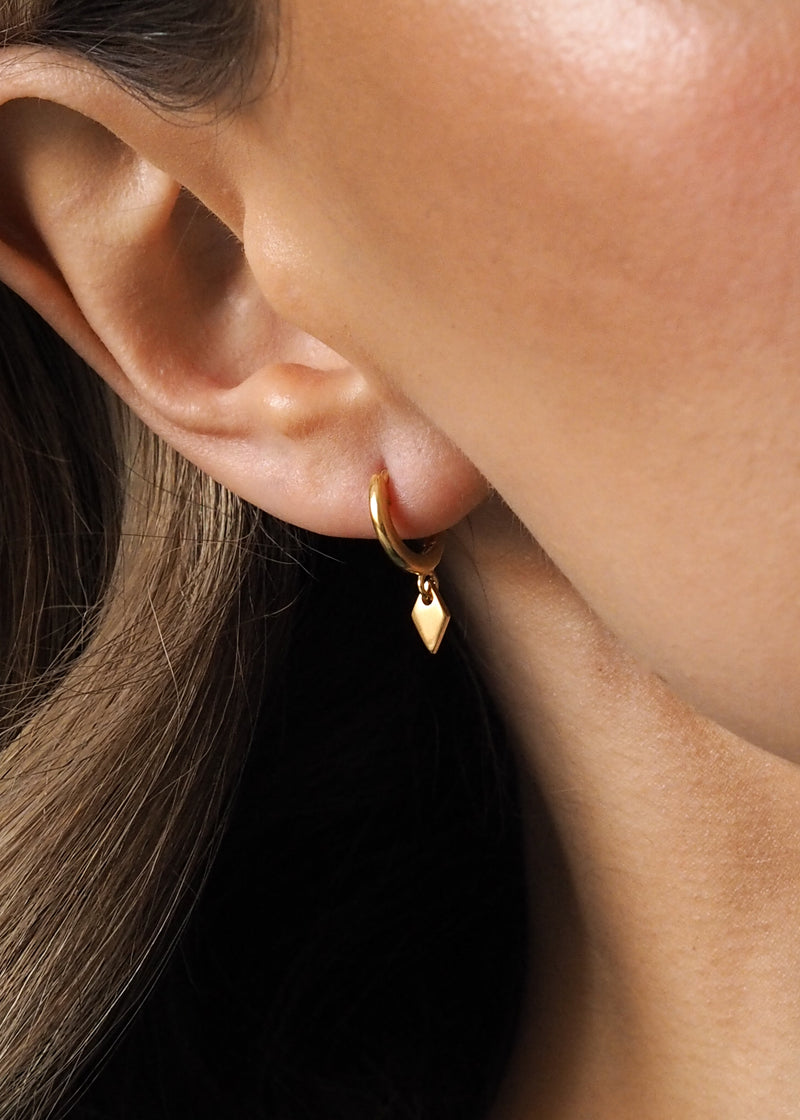 Close-up of a model wearing gold hoops with a small diamond-shaped drop pendant.