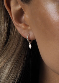 Close-up of a model wearing sterling silver hoops with a small diamond-shaped drop pendant.