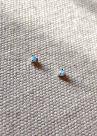 Pair of October birthstone opal gemstone stud earrings set in sterling silver, displayed on a textured cream fabric background.