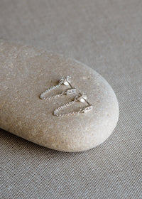 Pair of sterling silver drop chain earrings with rectangular cubic zirconia studs, displayed on a smooth neutral-toned stone.