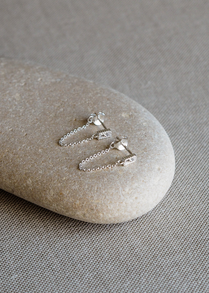 Pair of sterling silver drop chain earrings with rectangular cubic zirconia studs, displayed on a smooth neutral-toned stone.